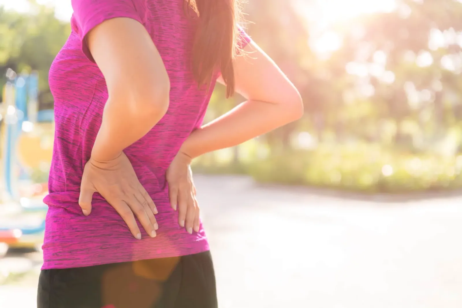 Woman in a pink shirt holding her lower back from sciatica pain outdoors